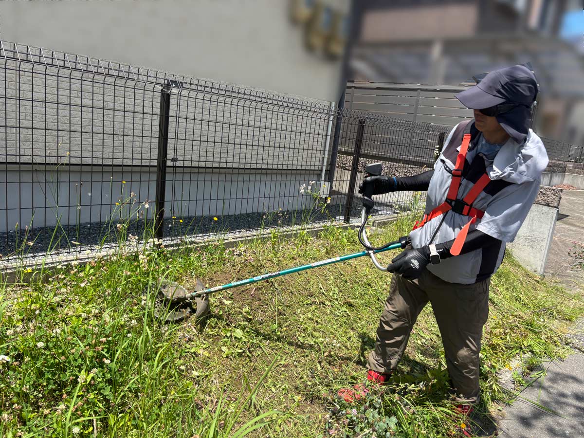 石巻市須江地区の貸家、フェンス沿いの伸びた雑草を電動刈払機で刈っている様子