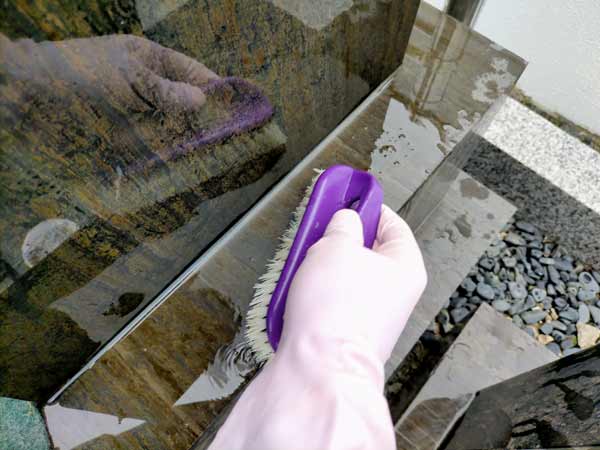 墓石掃除ブラシを使い墓石の水洗い作業中の写真