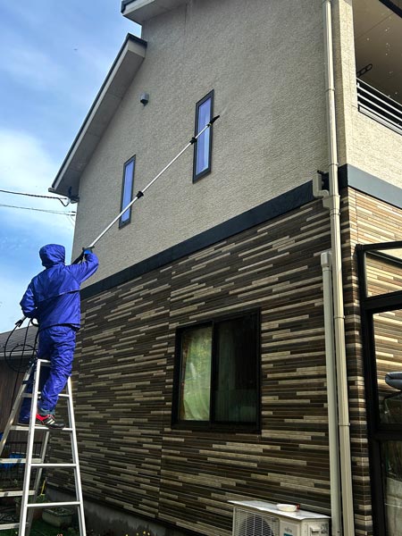 便利屋フォーカスの外壁掃除・外壁洗浄サービス（脚立に乗り戸建て住宅の外壁2階部分の高所を高圧洗浄機ケルヒャーを使いカビ汚れ、コケ汚れ、黒ずみ汚れを清掃中の様子）